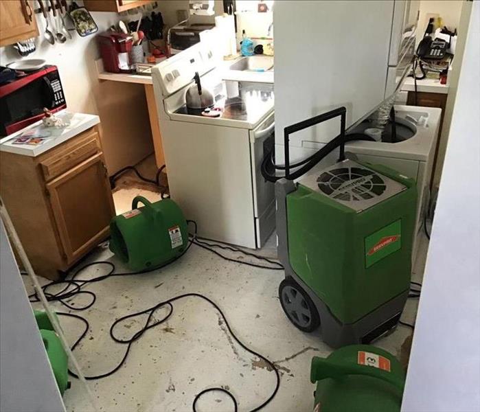 Kitchen with removed floors, detached appliances, and SERVPRO branded large capacity dehumidifier/ air movers neatly arranged